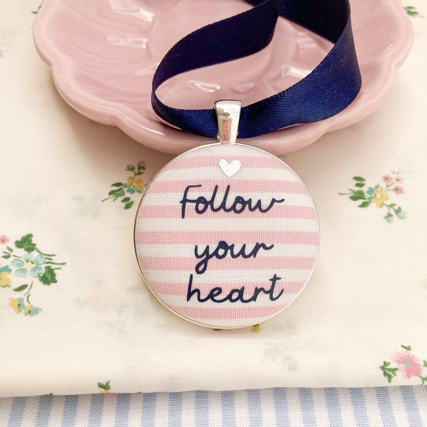 Keepsake with Follow Your Heart printed onto pink & white striped fabric, hanging on a navy blue ribbon