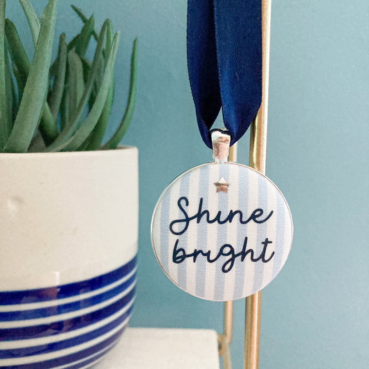 Keepsake with the words Shine Bright printed on blue and white striped fabric with a navy blue ribbon