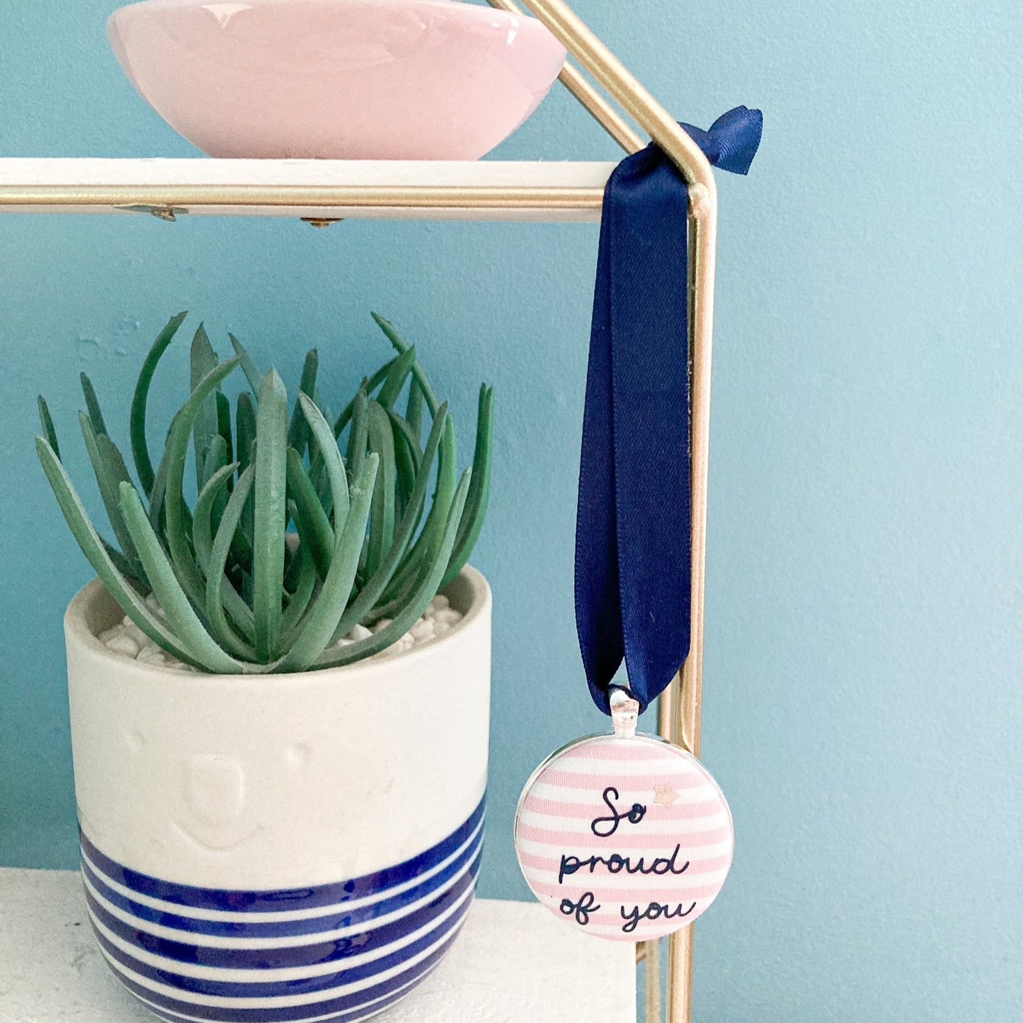 Keepsake with So Proud Of You printed onto pink and white striped fabric with a navy blue ribbon
