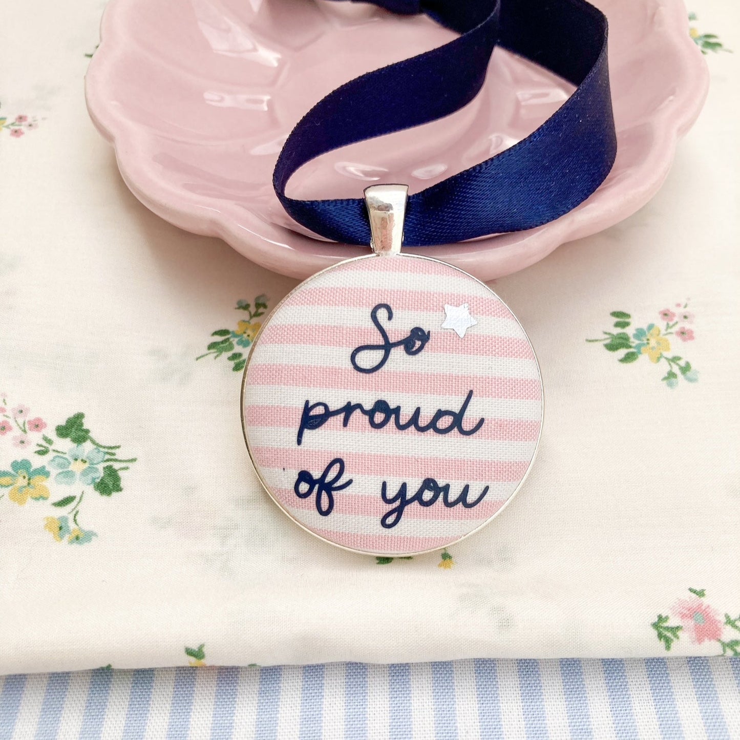 Keepsake with So Proud Of You printed onto pink and white striped fabric with a navy blue ribbon