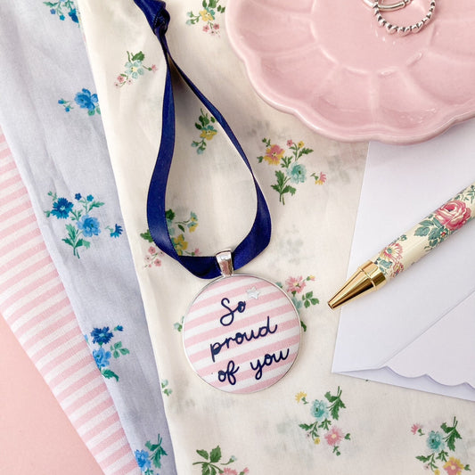 Keepsake with So Proud Of You printed onto pink and white striped fabric with a navy blue ribbon