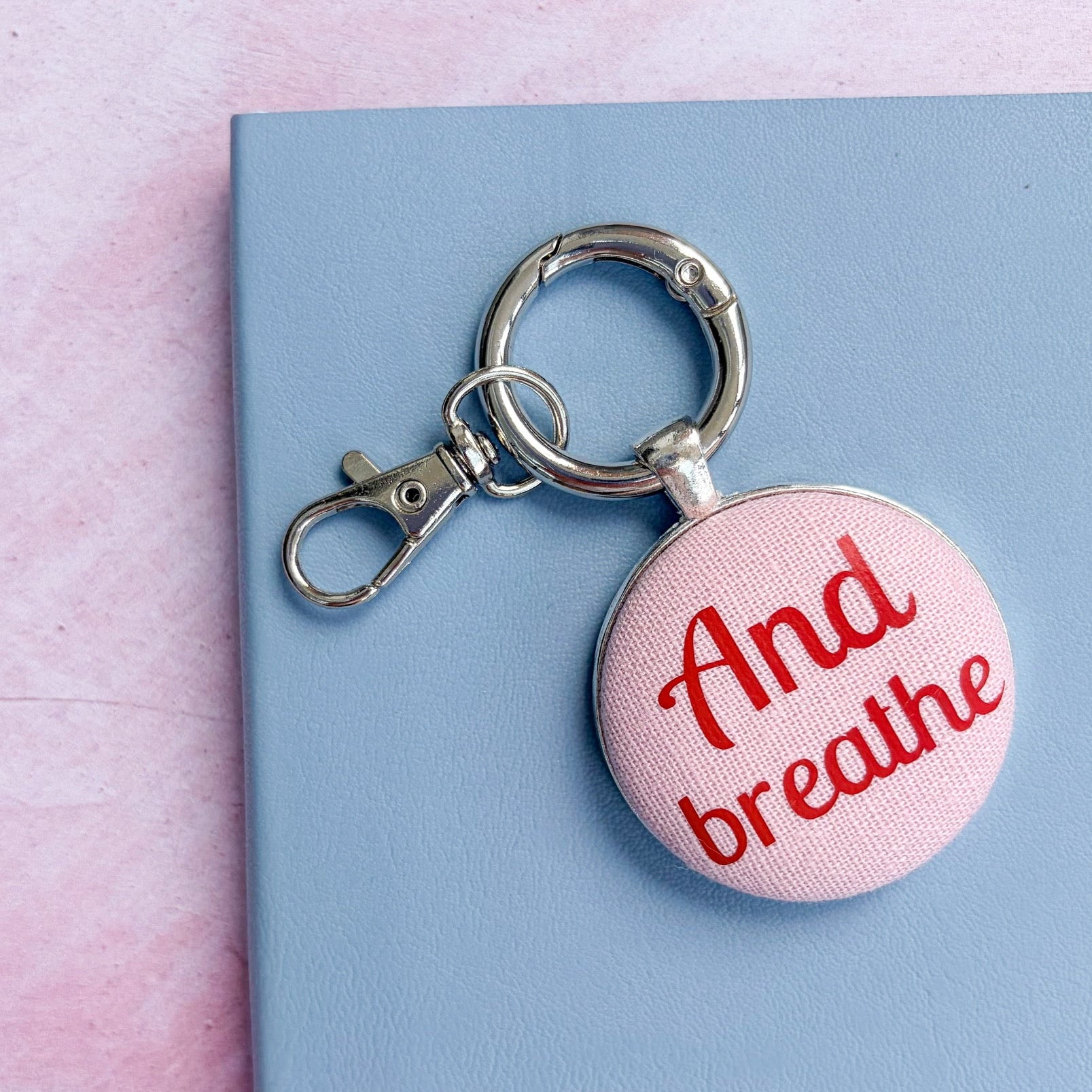 Keyring with 'And breathe' text on pink fabric set on a pink and blue background 