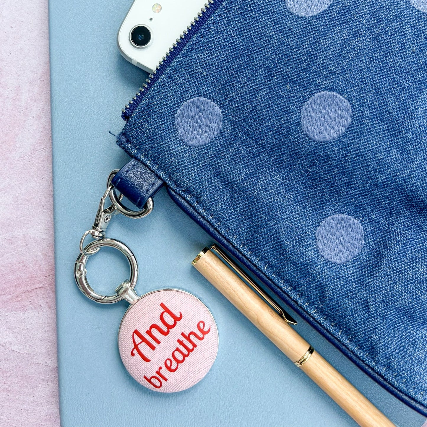 Blue polka dot pouch with a phone, pen, and "And Breathe" keyring on a light blue background