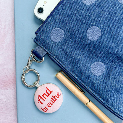 Blue polka dot pouch with a phone, pen, and "And Breathe" keyring on a light blue background