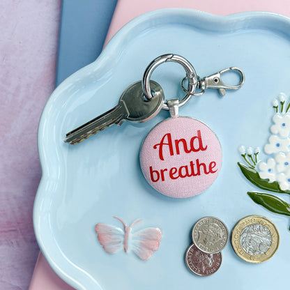 Keyring with 'And breathe' charm on a decorative plate with coins and keys
