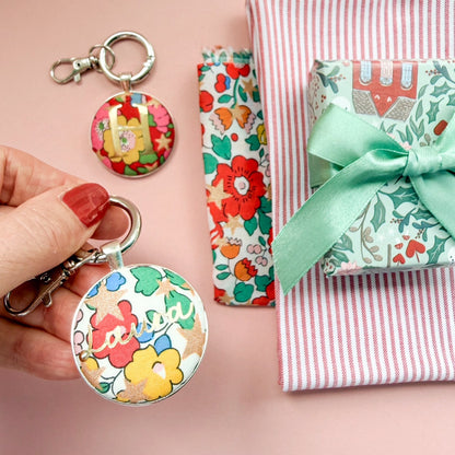 Floral Christmas keyrings with names and initials in gold next to floral and striped fabrics and a small gift