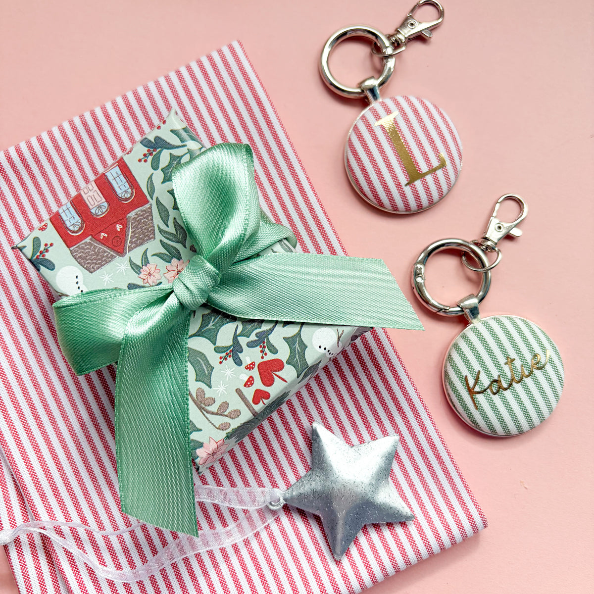 Personalized round keychains with silver keyrings and clasps, displayed on a red striped fabric. One keychain has a red and white striped button with a gold monogram 'L', and the other has a green and white striped button with a gold monogram 'Katie'.