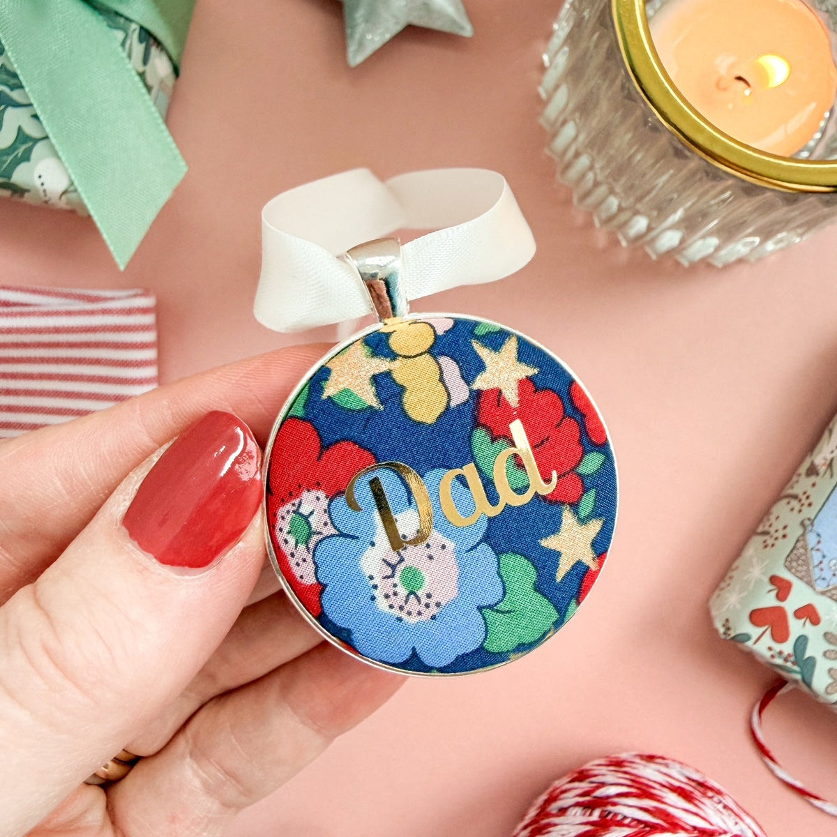 Personalised Christmas keepsake or memory keepsake with dad printed in gold foil, made with blue floral and star Liberty fabric, in a silver plated setting, thread on white satin ribbon, on a Christmas flatlay