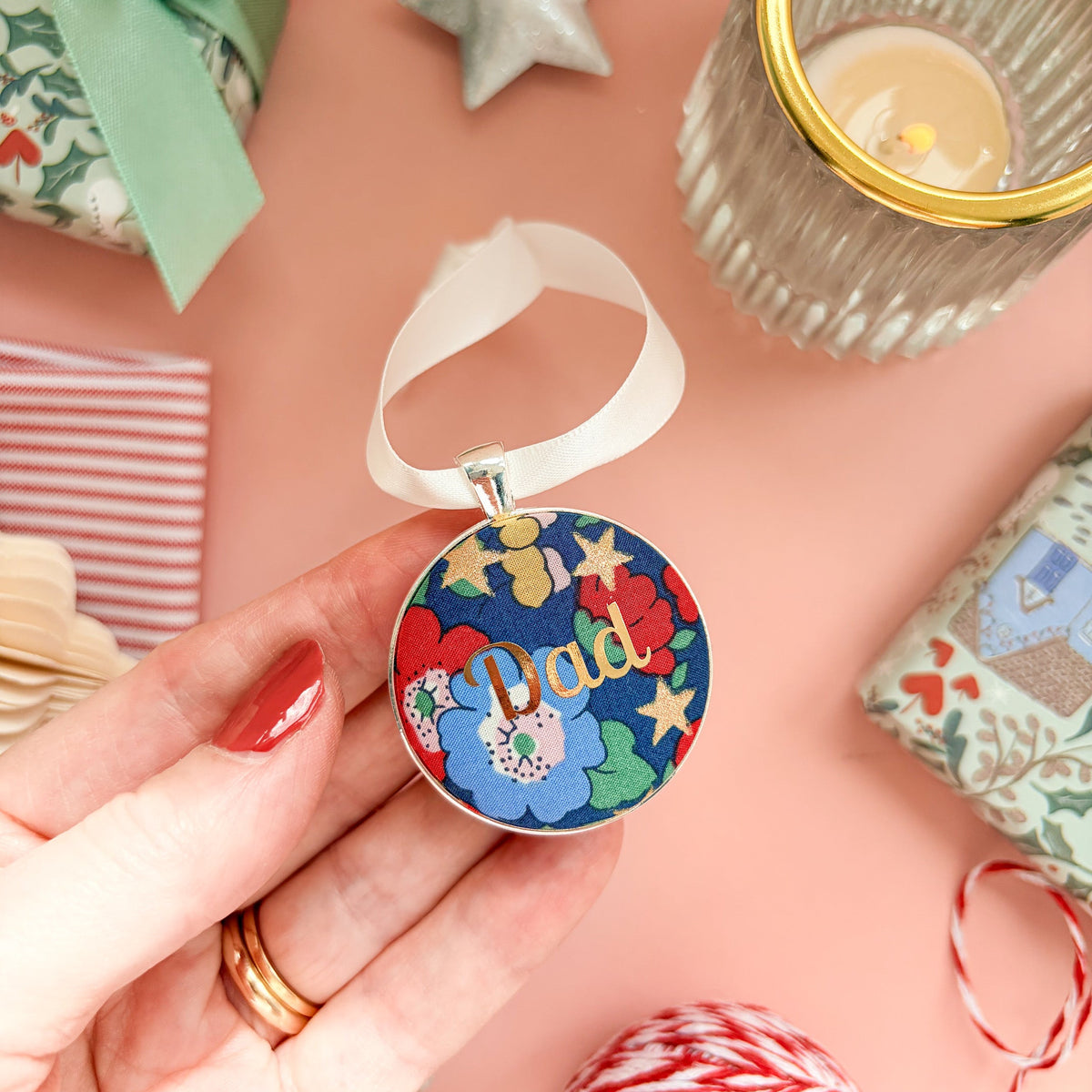 Personalised Christmas keepsake or memory keepsake with dad printed in gold foil, made with blue floral and star Liberty fabric, in a silver plated setting, thread on white satin ribbon, on a Christmas flatlay