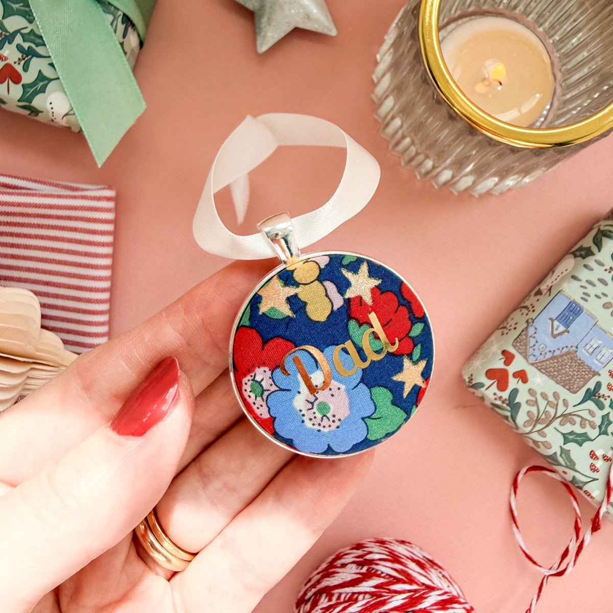 Personalised Christmas keepsake or memory keepsake with dad printed in gold foil, made with blue floral and star Liberty fabric, in a silver plated setting, thread on white satin ribbon, on a Christmas flatlay