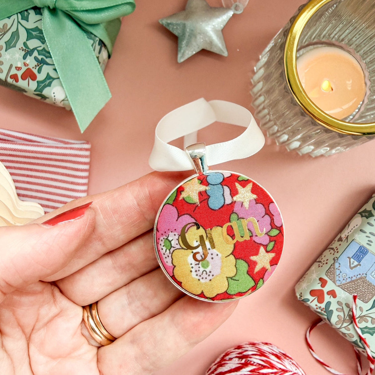 A Christmas personalised keepsake or memory keepsake, with gran printed in gold foil, on Liberty red floral fabric, thread on an ivory ribbon, and set on a Christmas flatlay