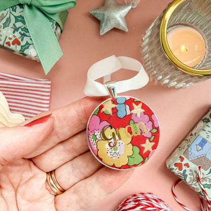 A Christmas personalised keepsake or memory keepsake, with gran printed in gold foil, on Liberty red floral fabric, thread on an ivory ribbon, and set on a Christmas flatlay