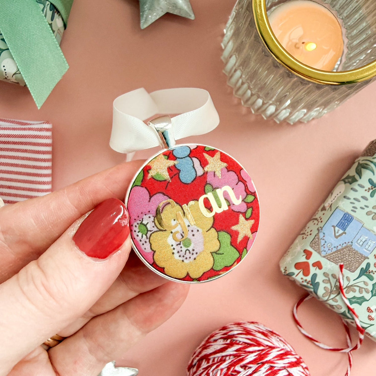 A Christmas personalised keepsake or memory keepsake, with gran printed in gold foil, on Liberty red floral fabric, thread on an ivory ribbon, and set on a Christmas flatlay