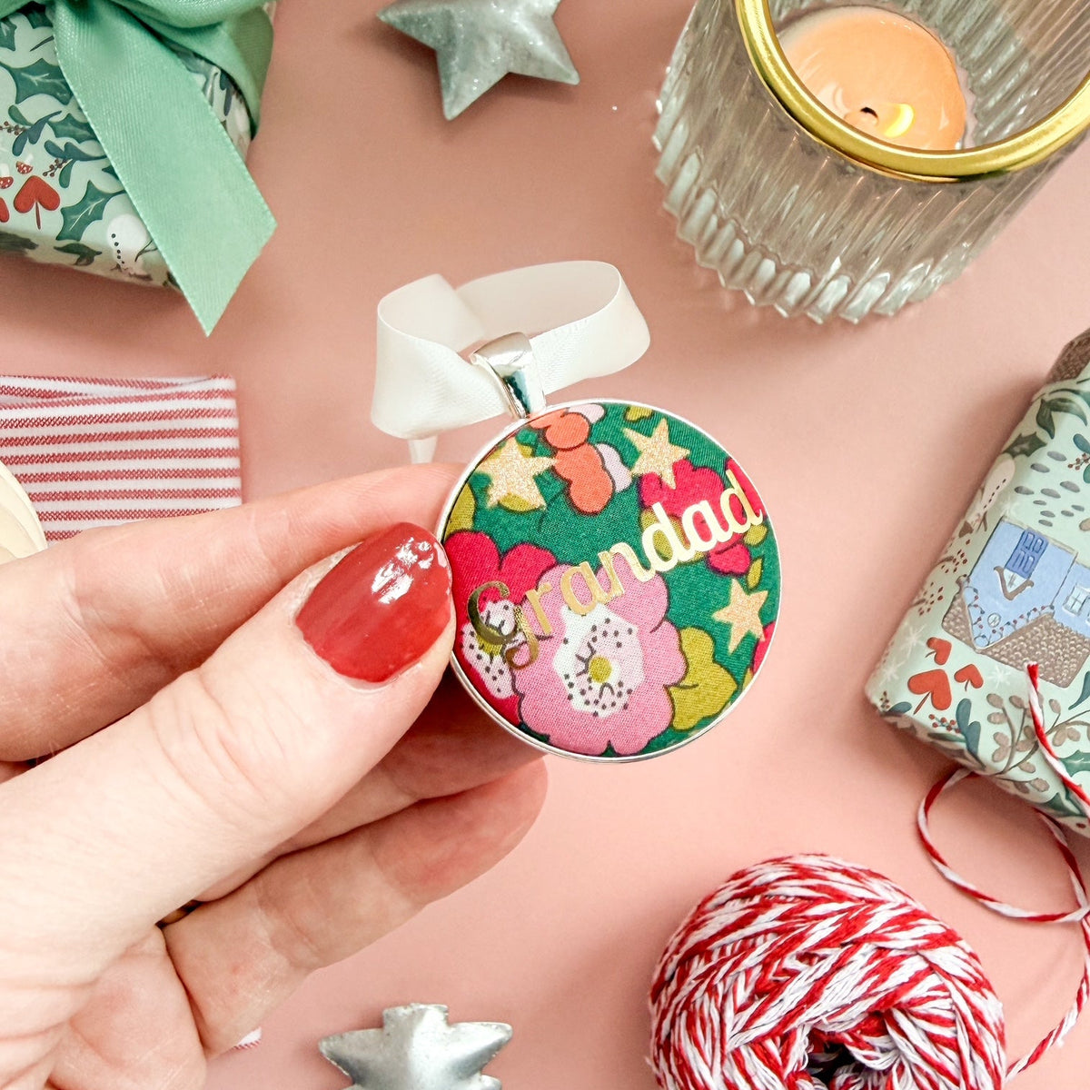 A Grandad Christmas keepsake or memory keepsake, made with green floral Liberty fabric, printed with Grandad in gold foil, set in silver plate, thread on a white satin ribbon, on a Christmas flatlay