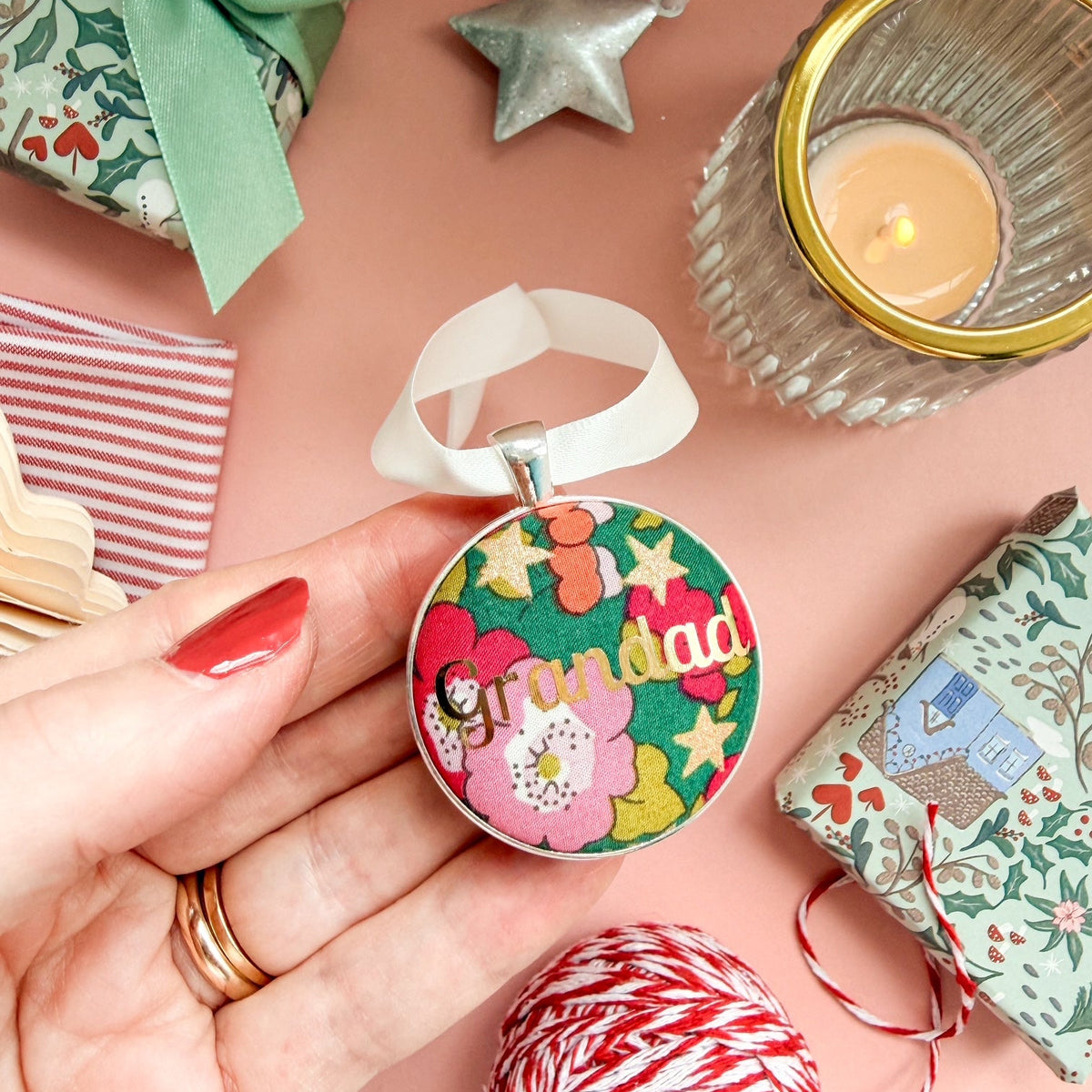 A Grandad Christmas keepsake or memory keepsake, made with green floral Liberty fabric, printed with Grandad in gold foil, set in silver plate, thread on a white satin ribbon, on a Christmas flatlay