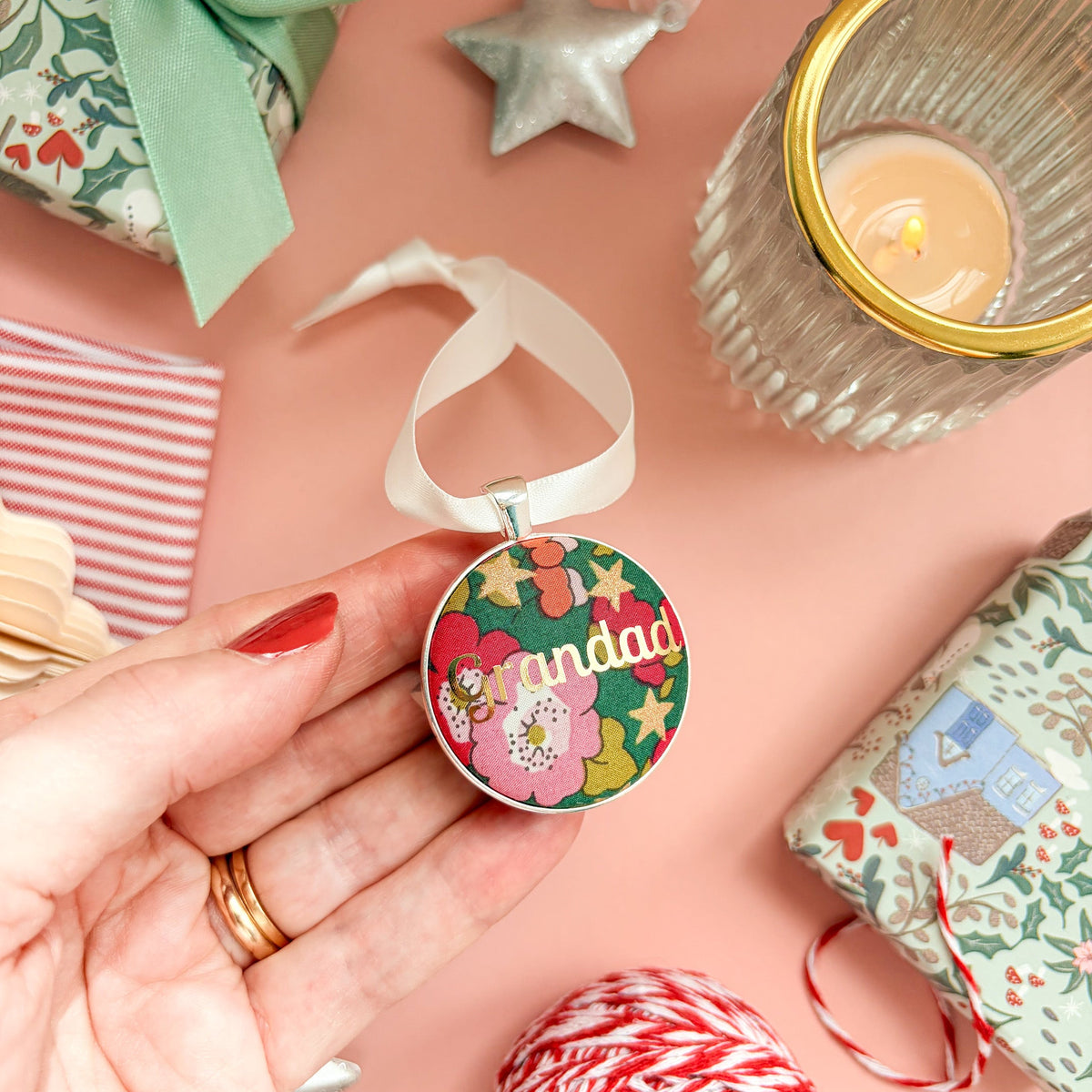 A Grandad Christmas keepsake or memory keepsake, made with green floral Liberty fabric, printed with Grandad in gold foil, set in silver plate, thread on a white satin ribbon, on a Christmas flatlay