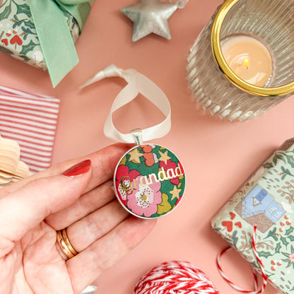 A Grandad Christmas keepsake or memory keepsake, made with green floral Liberty fabric, printed with Grandad in gold foil, set in silver plate, thread on a white satin ribbon, on a Christmas flatlay