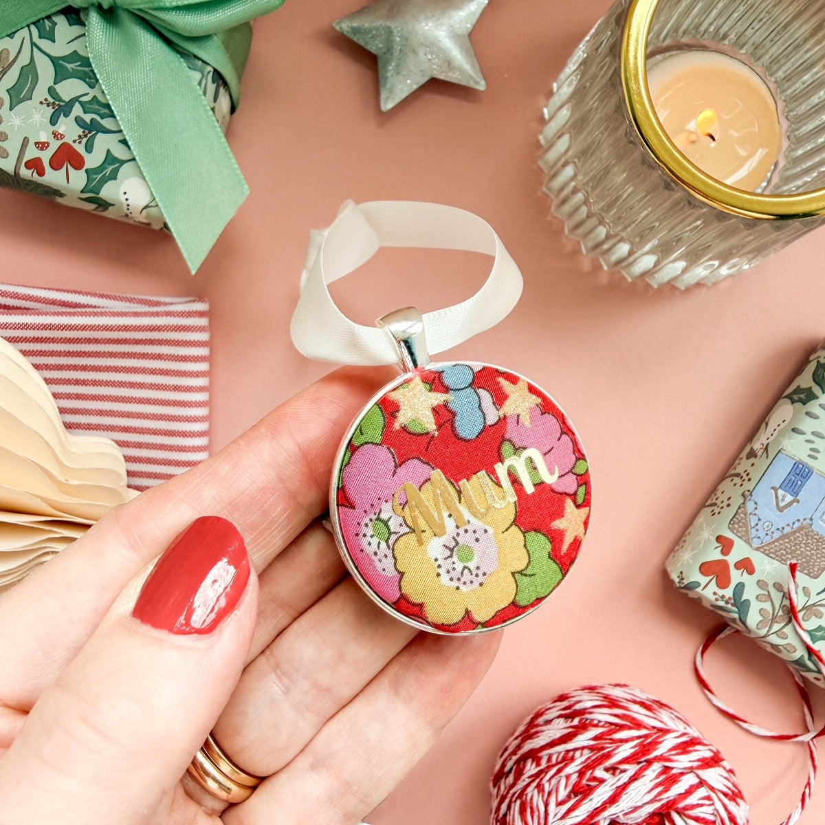 A Christmas Keepsake gift or memory keepsake, made with red floral Liberty fabric, printed with Mum in gold, thread on an ivory white ribbon and set on a Christmas flatlay