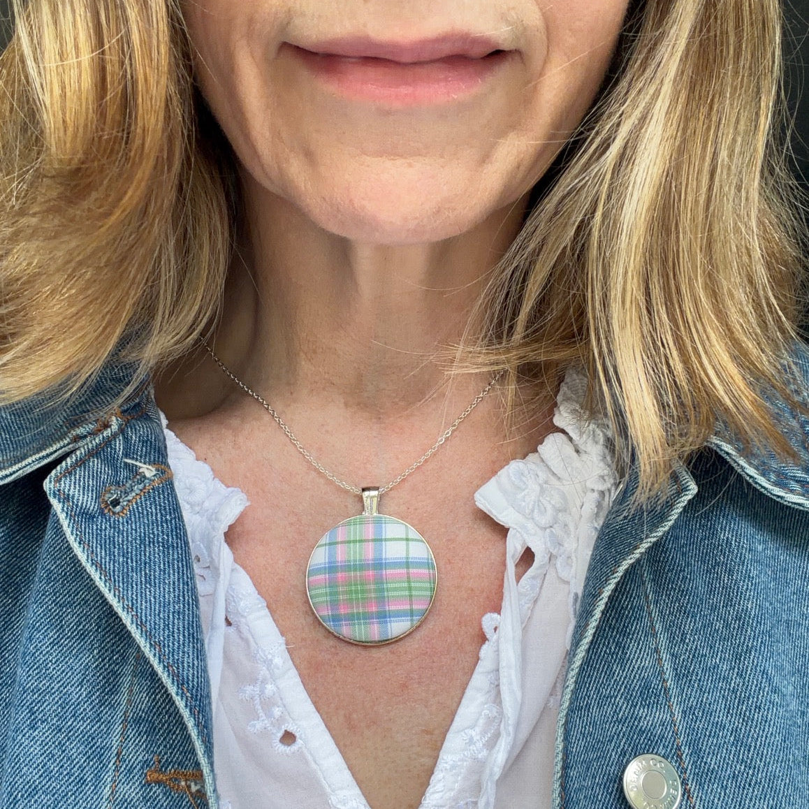 Person wearing a colorful checked pendant necklace with a denim jacket and white blouse.