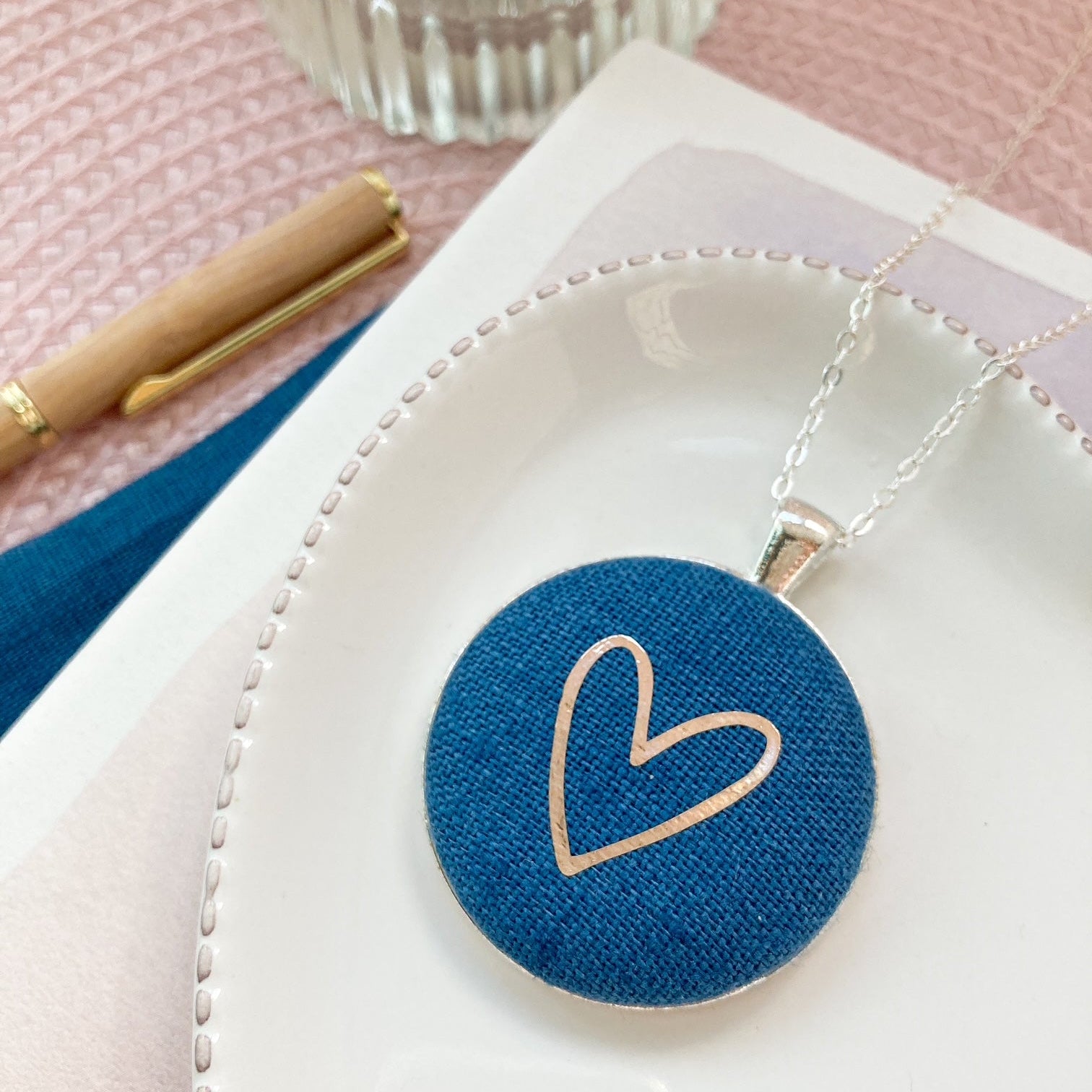 Blue heart-shaped pendant on a white dish with a pink background