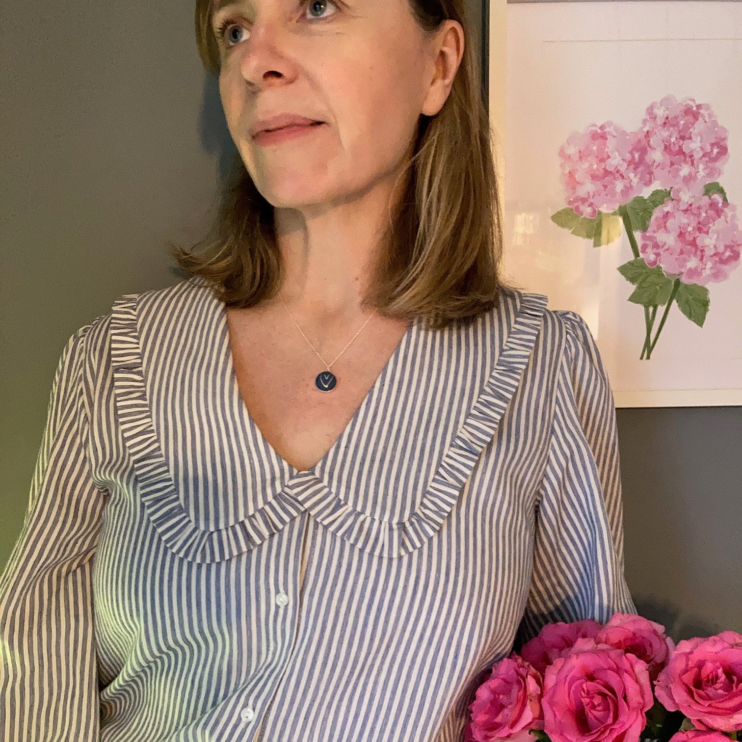 Person wearing a blue and gold heart necklace and striped shirt with pink flowers in the background