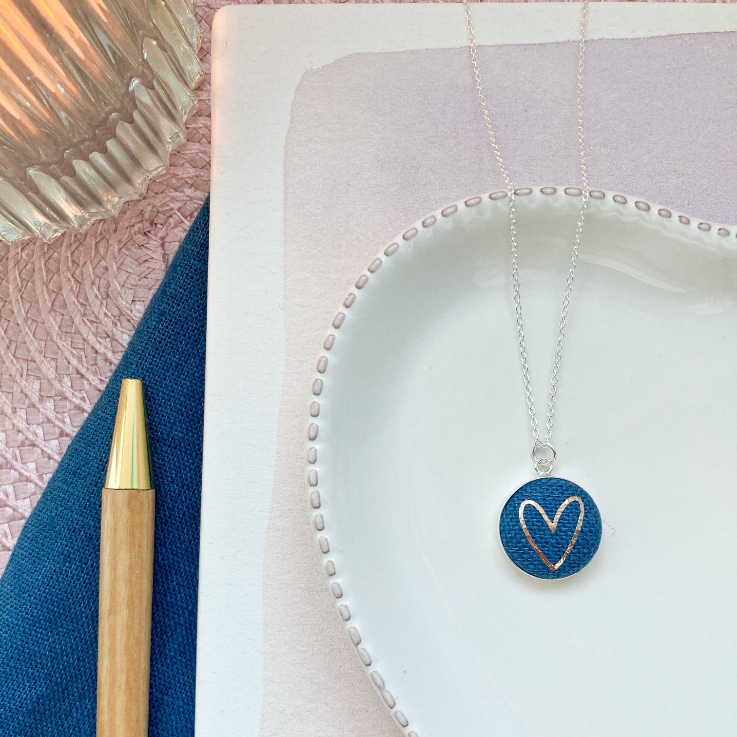 Necklace with a heart pendant on a textured surface next to a pen