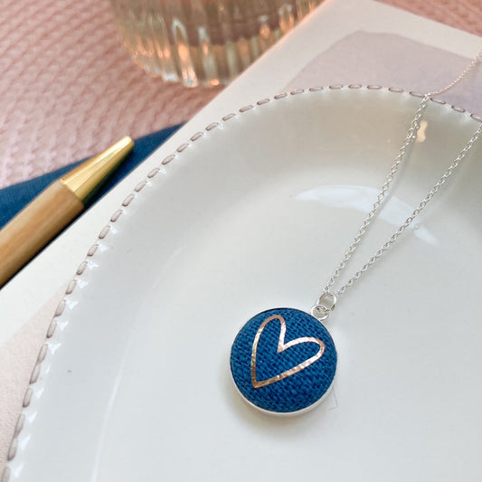 Necklace with a blue pendant featuring a heart design on a white surface.