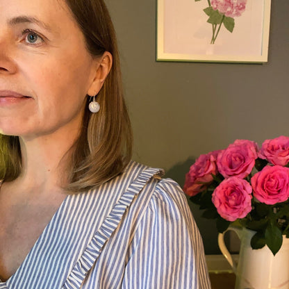 Woman wearing a striped shirt and heart earrings with a vase of pink roses in the background