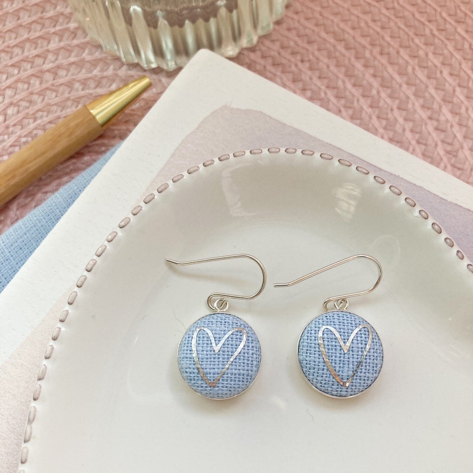 Earrings with heart design on a white dish with a pink background