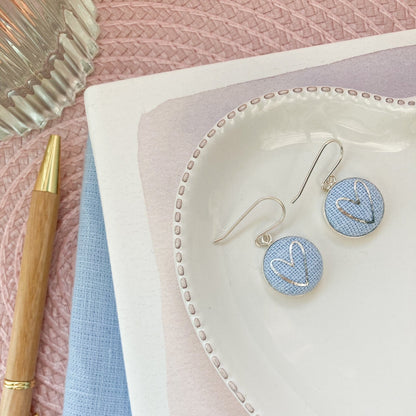 Earrings on a heart-shaped dish with a pen and fabric in the background