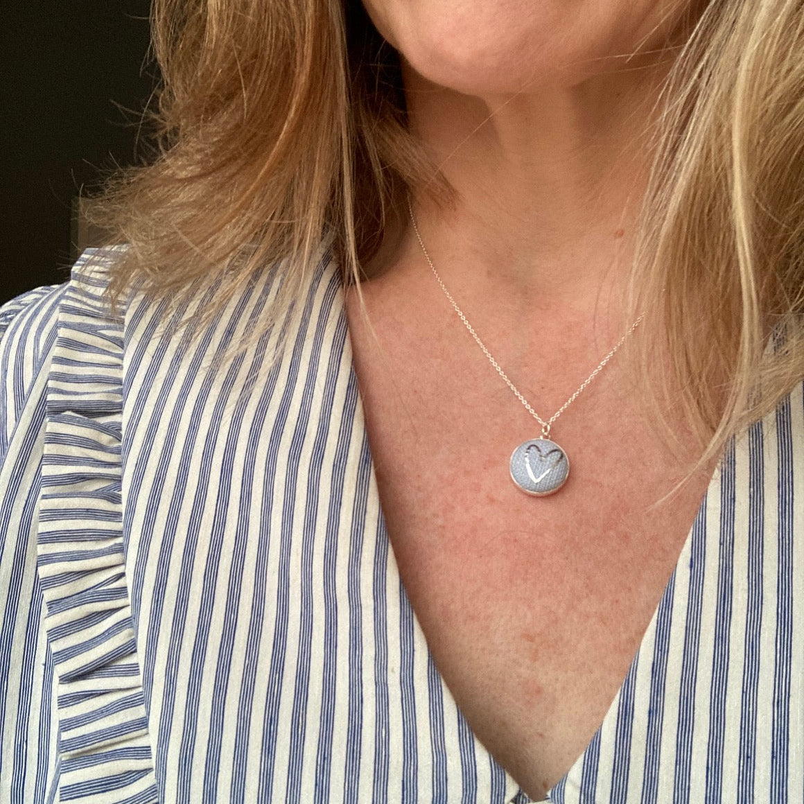 Close-up of a person wearing a blue heart necklace and a striped shirt.