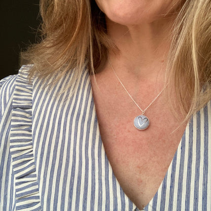 Close-up of a person wearing a blue heart necklace and a striped shirt.