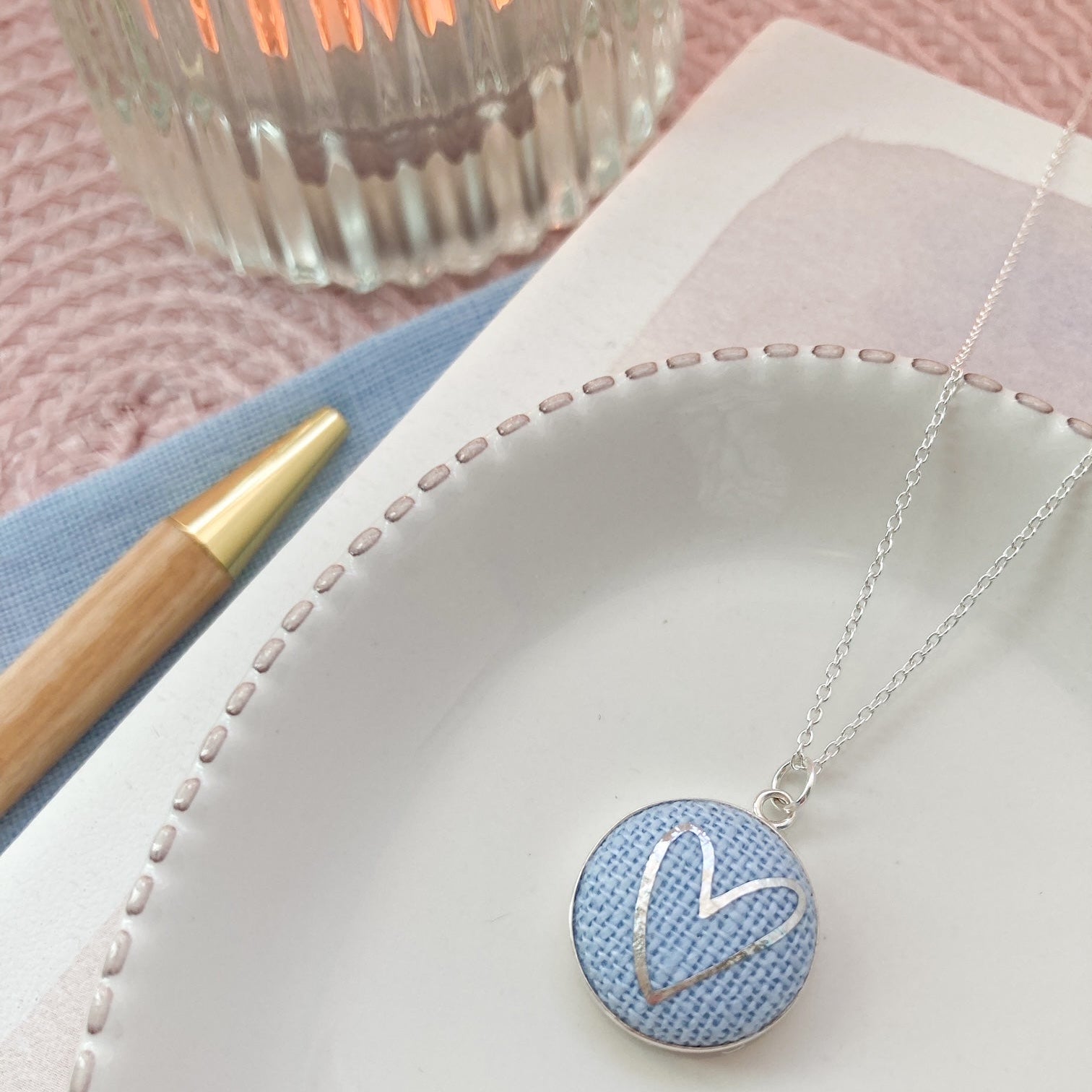 Necklace with a blue pendant on a white plate with a pink background