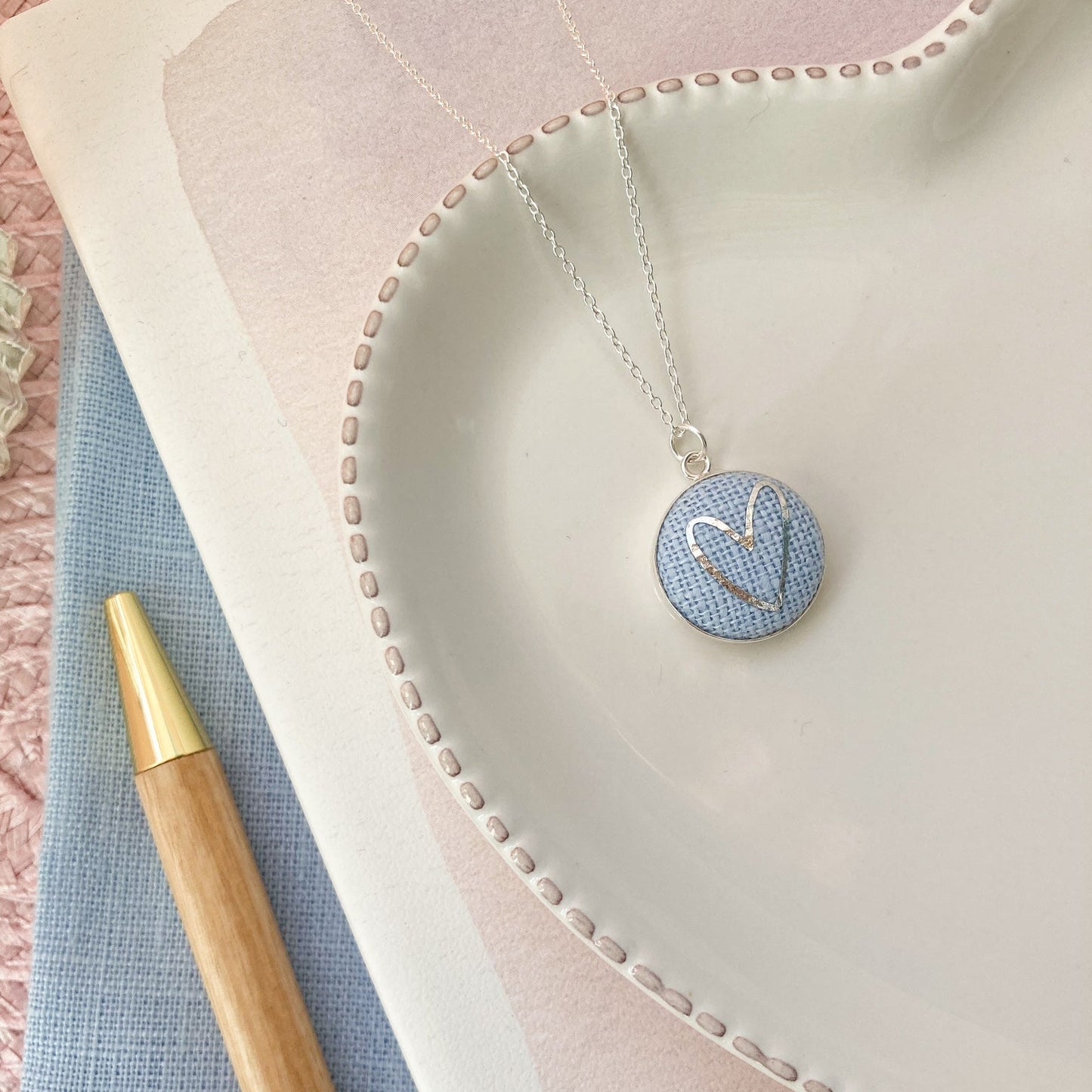 Necklace with a heart pendant on a textured fabric surface next to a pen