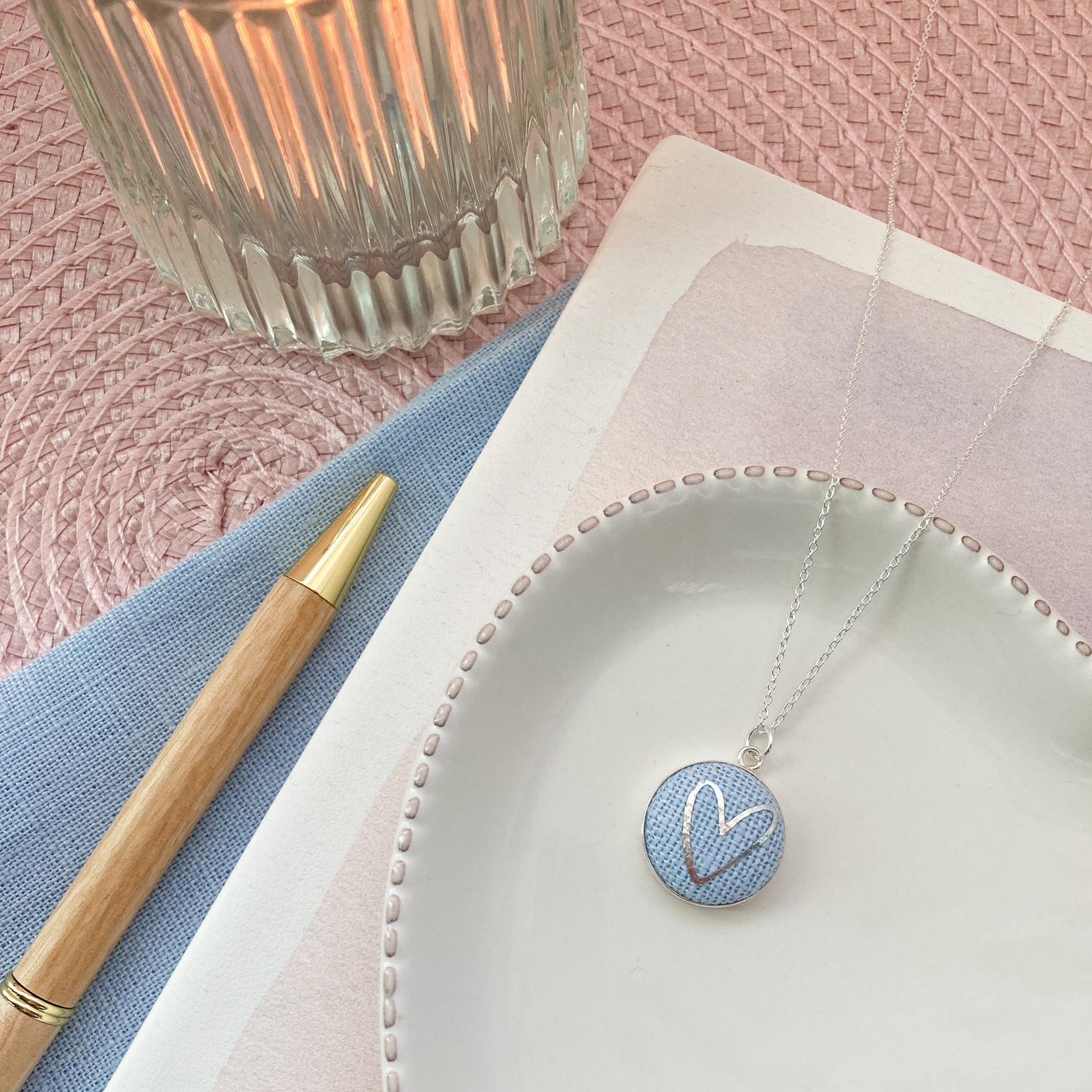 Necklace with a blue pendant on a white plate with a pink background