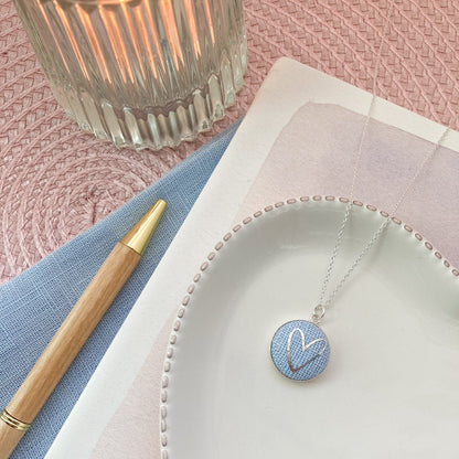 Necklace with a blue pendant on a white plate with a pink background