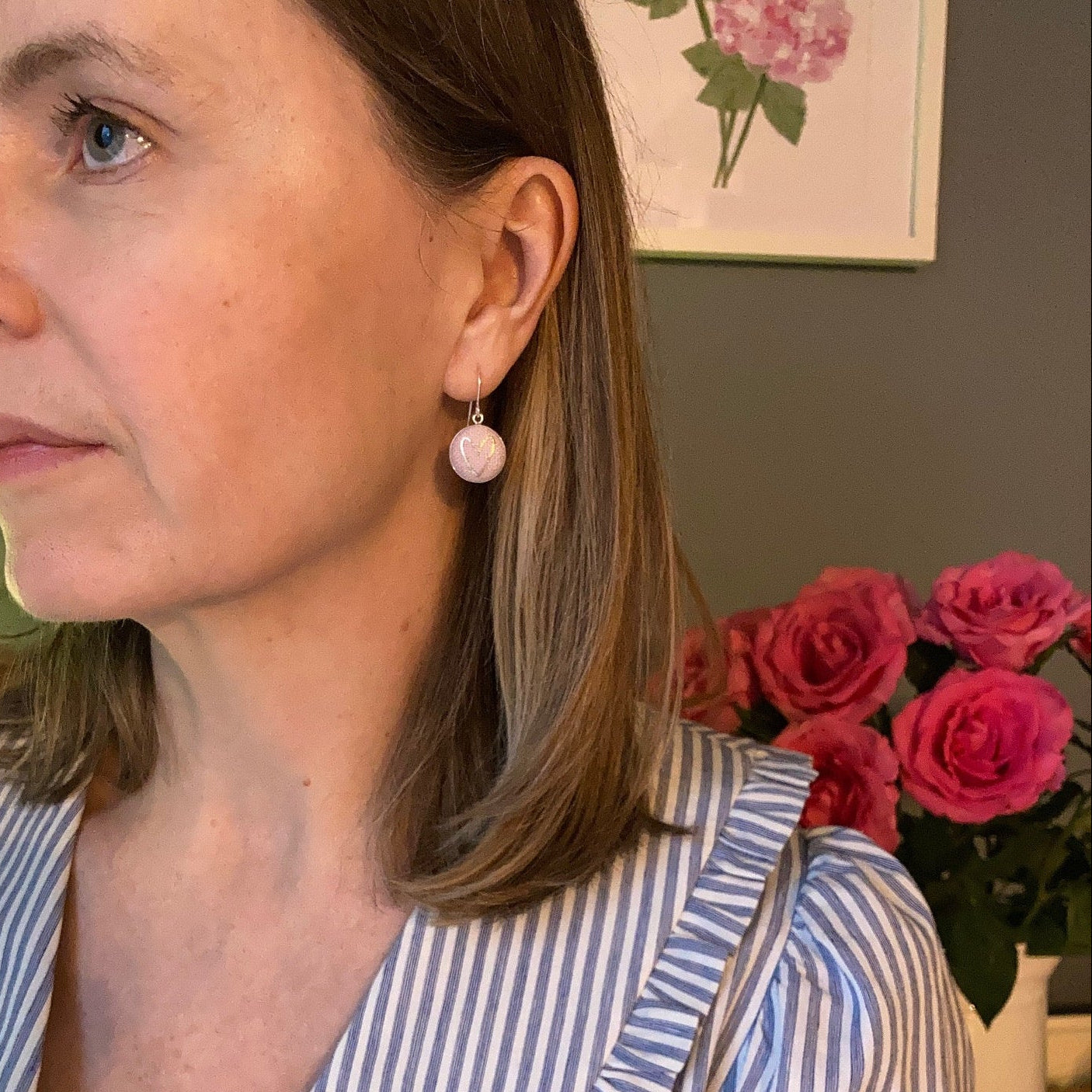 Person wearing a striped shirt and pink and gold heart earrings and flowers in the background