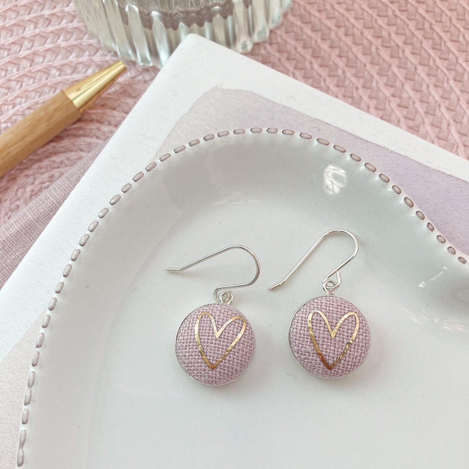 Pink earrings with gold heart design on a white dish with a pink background