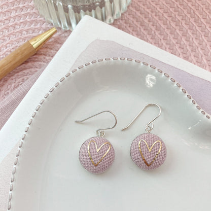 Pink earrings with gold heart design on a white dish with a pink background