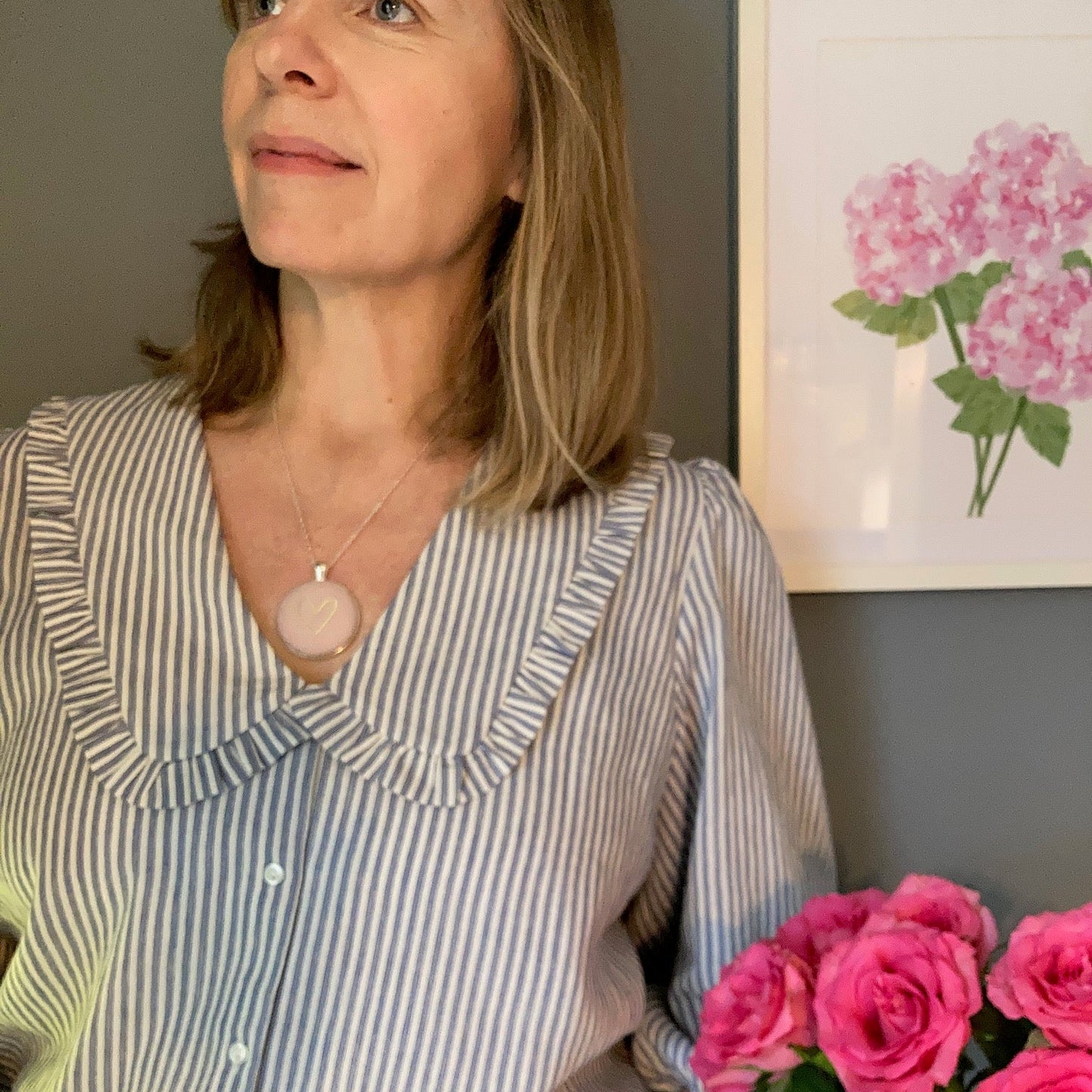 Woman wearing a pink & gold heart pendant and a striped shirt