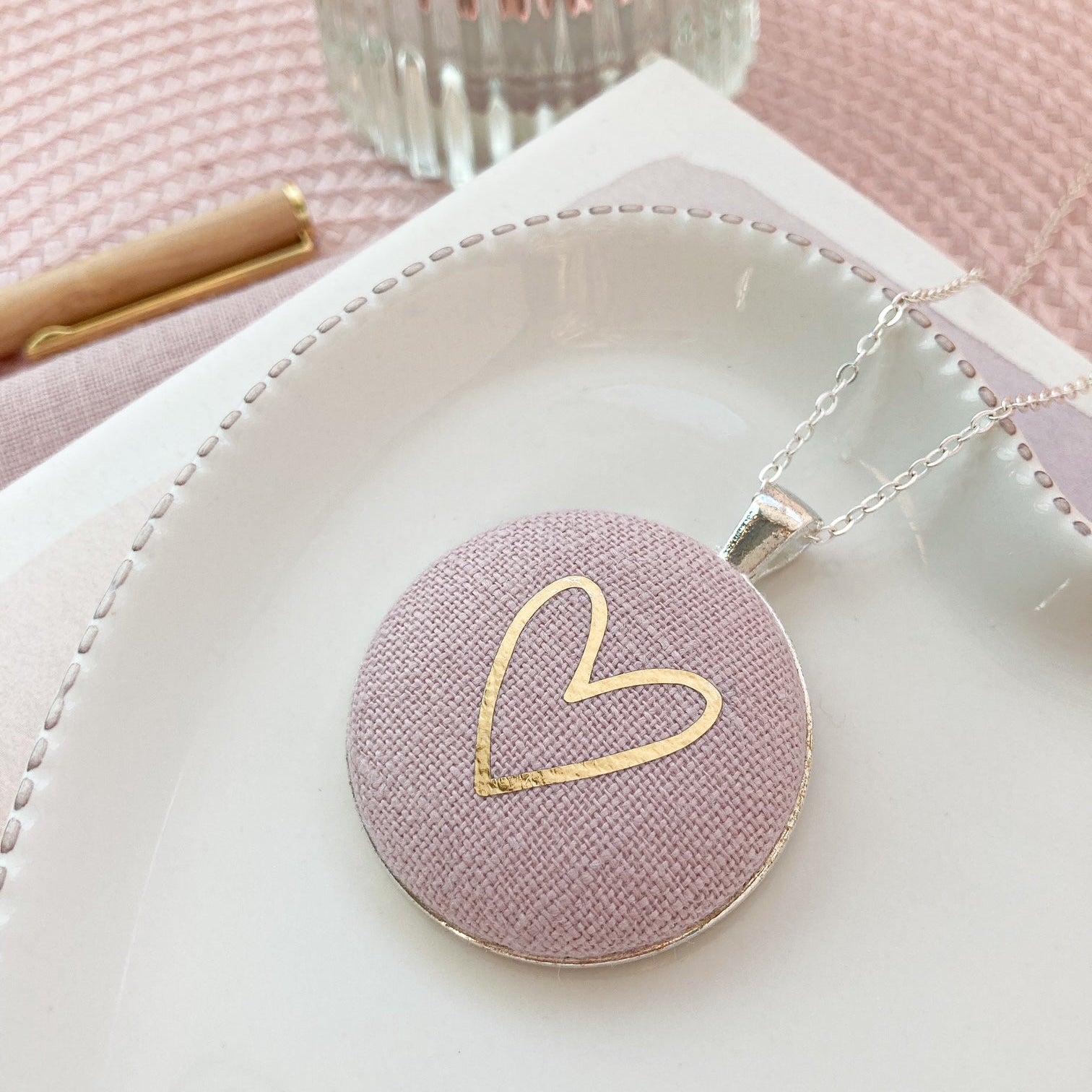 Necklace with pink pendant and gold heart design on a white surface.