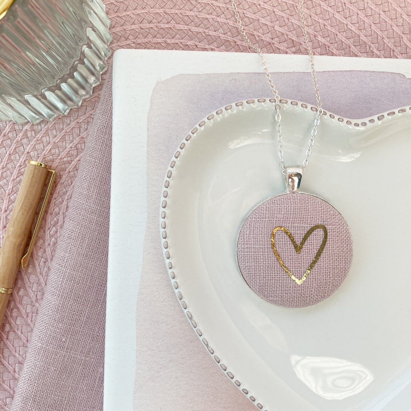 Heart-shaped dish with a necklace featuring a heart pendant on a pink textured surface.