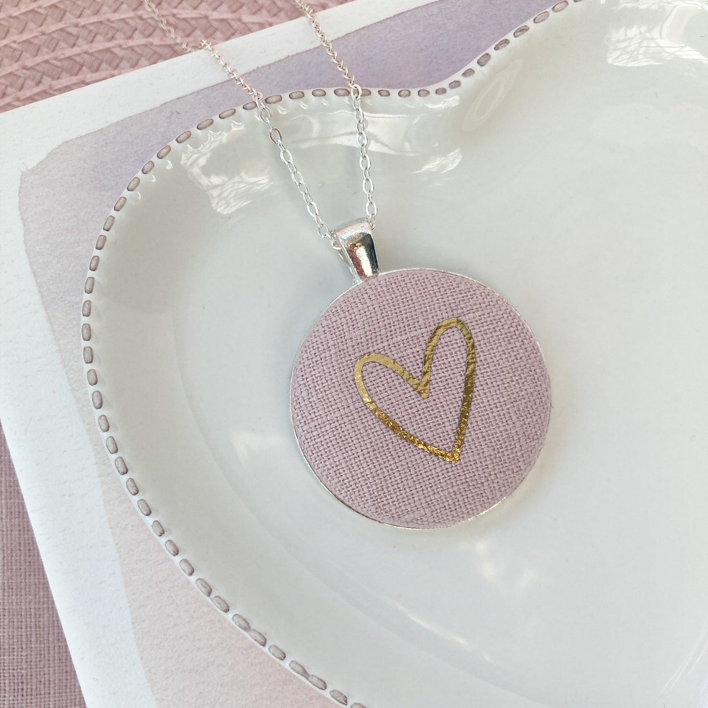 Necklace with a pink pendant featuring a gold heart design on a white dish.