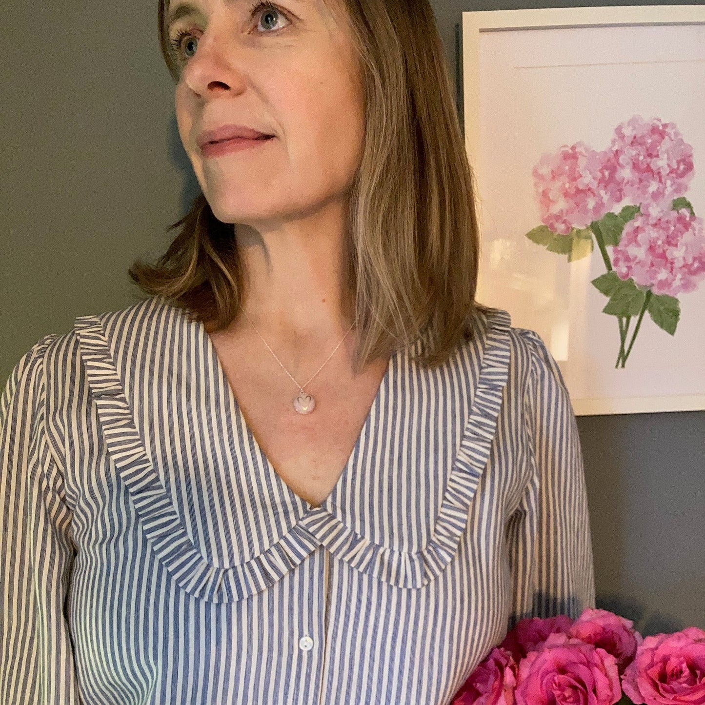 Person wearing a pink heart necklace and a striped shirt with pink flowers in the background