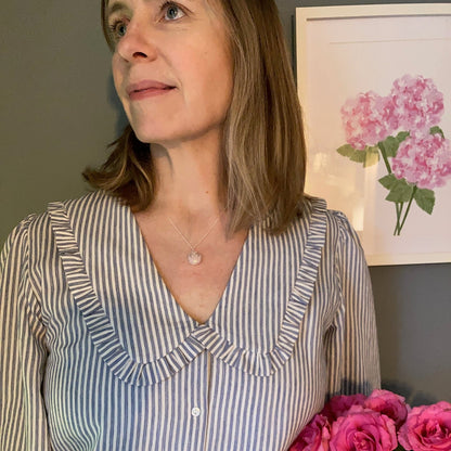 Person wearing a pink heart necklace and a striped shirt with pink flowers in the background