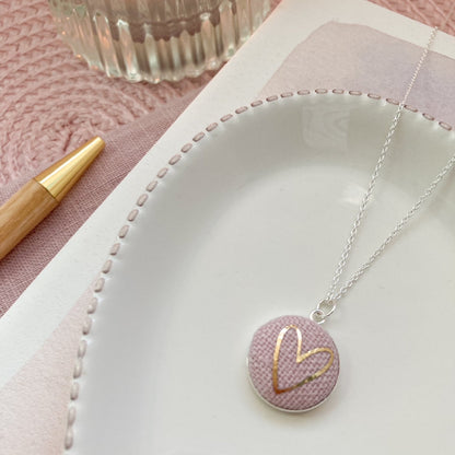Necklace with a pink pendant featuring a gold heart on a white dish with a pink background.