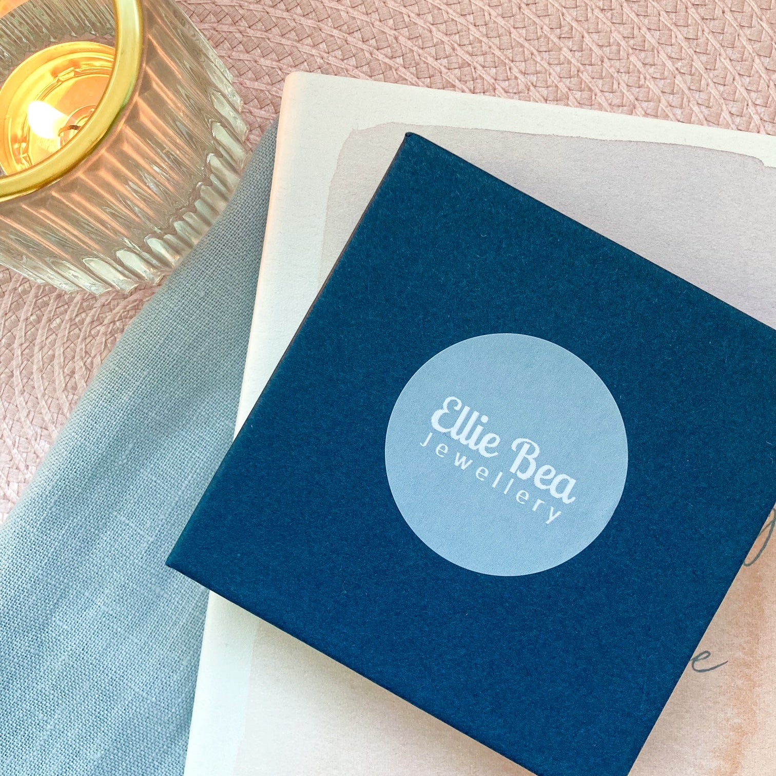 Blue jewelry box with 'Ellie Bea Jewellery' logo on a soft pink background