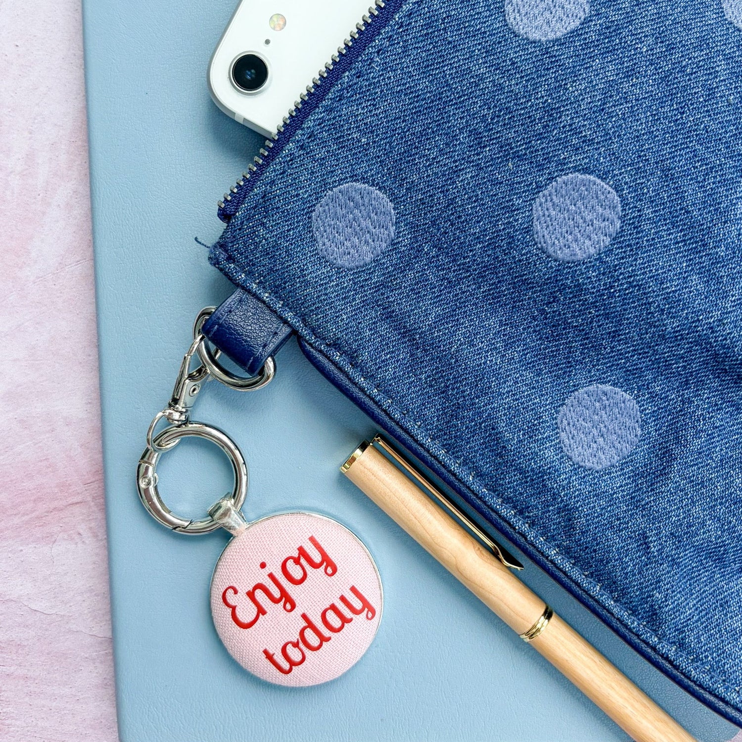 Blue polka dot pouch with an "Enjoy Today" red and pink keyring and phone on a light blue background