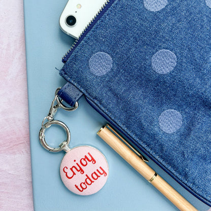 Blue polka dot pouch with an "Enjoy Today" red and pink keyring and phone on a light blue background