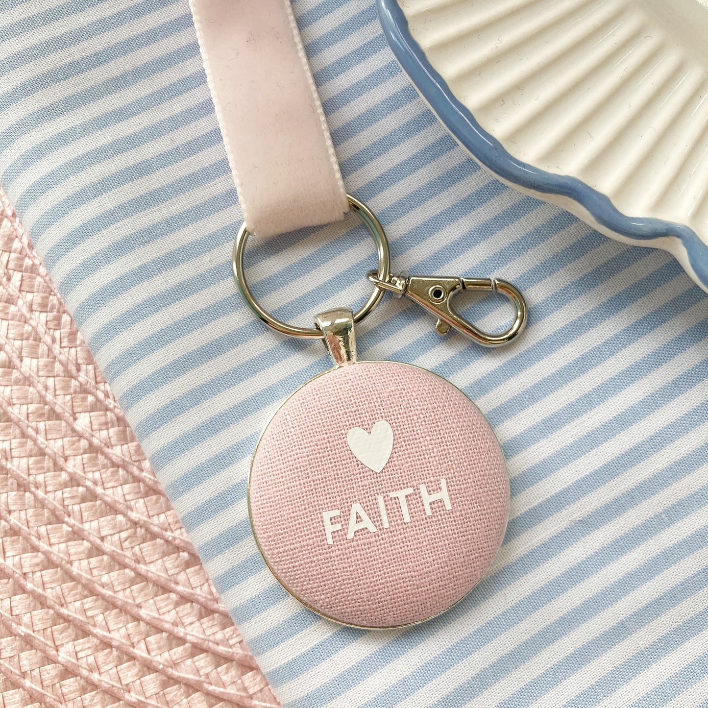 Pink fabric key ring with 'FAITH' and a heart, on a striped fabric background